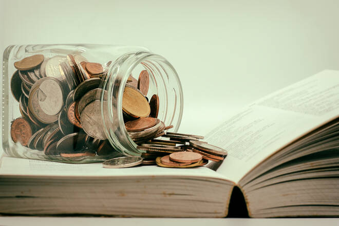 Glass jar of coin on opened book with dark background
