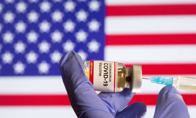 A small bottle labeled with a "Coronavirus COVID-19 Vaccine" sticker and a medical syringe in front of displayed USA flag in this illustration