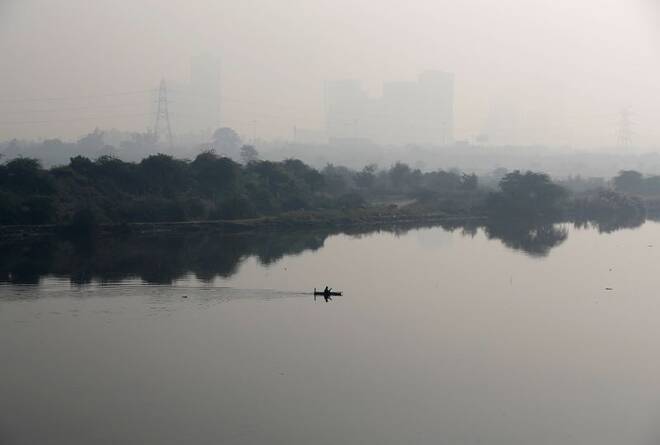 A man rows a boat as buildings shrouded in smog are seen in the background on the outskirts of Delhi