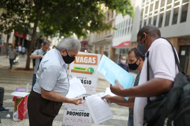Men deliver resumes near a job listing on a board reading "Vacancies" in downtown Sao Paulo