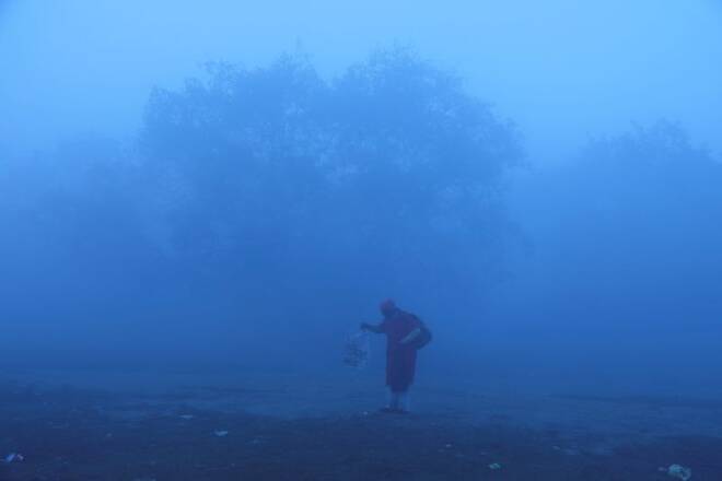 A man holds a newspaper on the banks of the Yamuna river on a smoggy morning in New Delhi