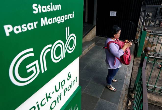 A woman uses her phone near a sign for the online ride-hailing service Grab at the Manggarai train station in Jakarta, Indonesia