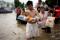 Man holding a baby wades through a flooded road following heavy rainfall in Zhengzhou