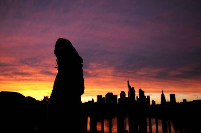 A woman wearing a protective mask walks past the skyline of the financial district during sunset as the spread of the coronavirus disease (COVID-19) continues in Frankfurt