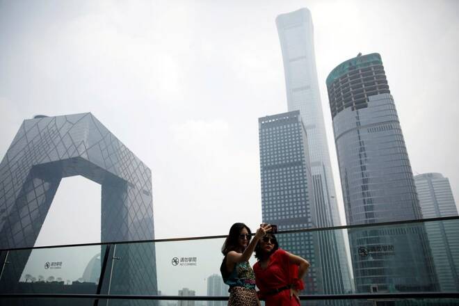 Women pose for pictures at a shopping mall near the CCTV headquarters and China Zun skyscraper in Beijing