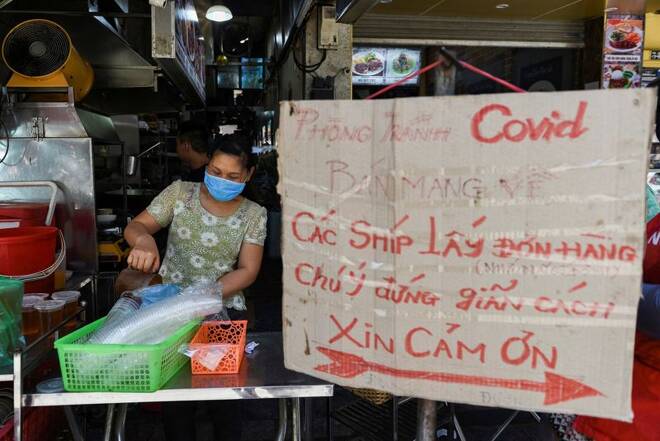 A woman sells food next to a banner reading "prevent the spread of COVID-19, take away only, please keep your distance 2 meters" amid the coronavirus disease (COVID-19) outbreak in Hanoi,