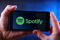 Hands holding smartphone displaying logo of Spotify