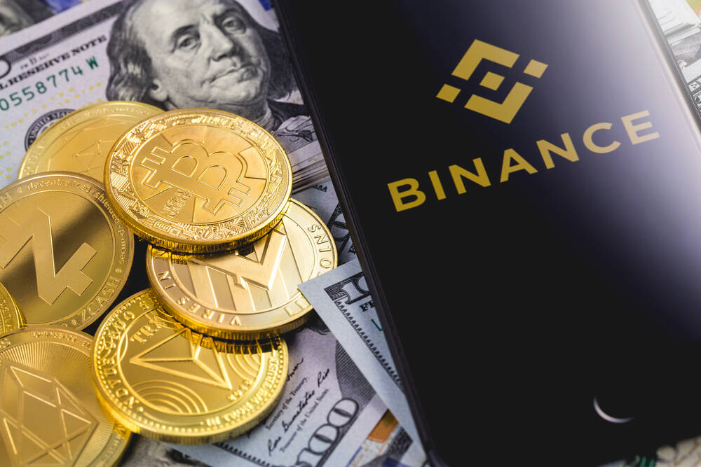 Apple iPhone and Binance logo, with dollars and cryptocurrency.
