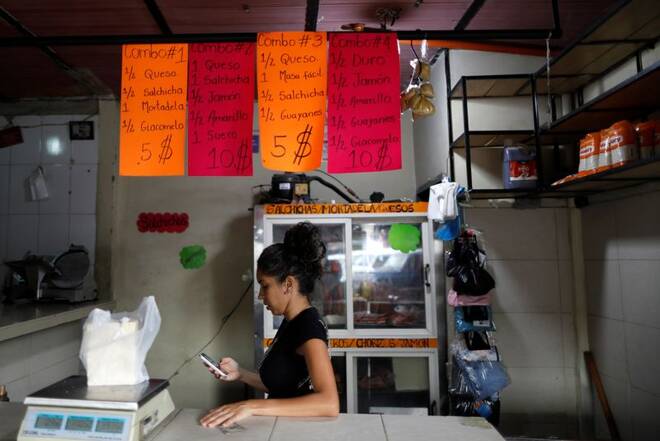 A worker checks her phone in a store that sells sausages in a market in Caracas