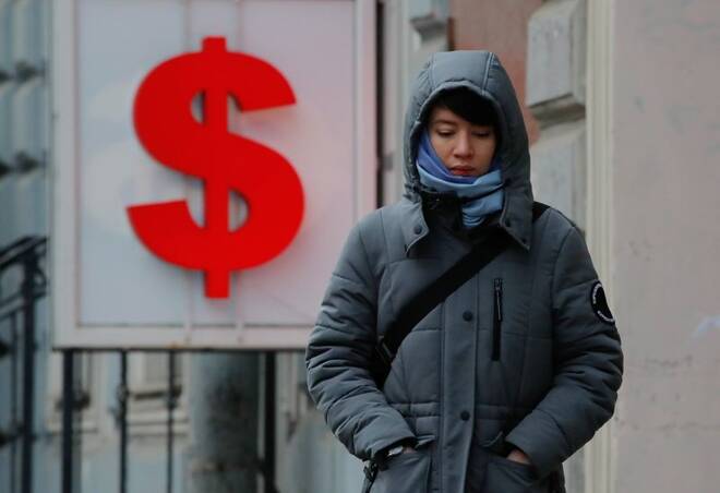 A woman walks past a board showing the U.S. dollar sign in a street in Saint Petersburg