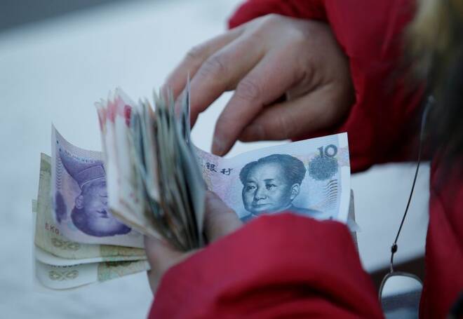 A woman counts Chinese Yuan banknotes as she sells tickets for a job fair in Beijing
