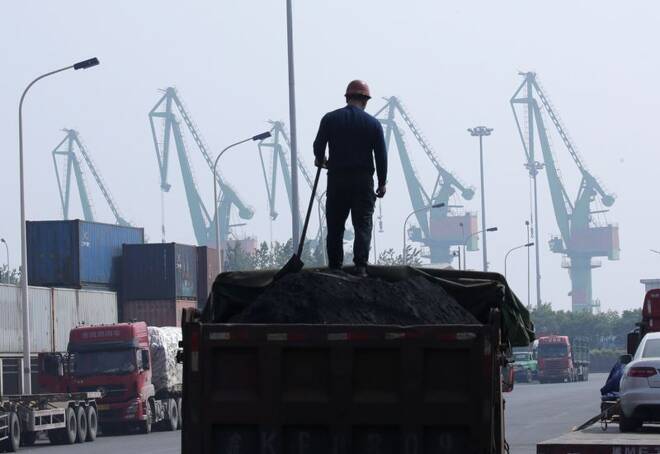 A labourer loads coal in a truck next to containers outside a logistics center near Tianjin Port