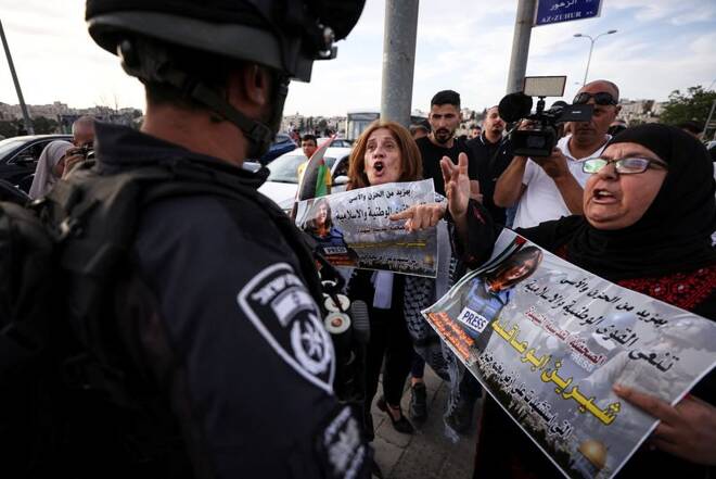 Palestinian protestors shout slogans towards Israeli police as they hold images of Al Jazeera reporter Shireen Abu Akleh, who was killed during an Israeli raid in Jenin in the occupied West Bank, near her house in Jerusalem