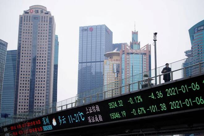 A man stands on an overpass with an electronic board showing Shanghai and Shenzhen stock indexes in Shanghai