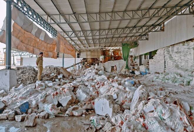 Police officers stand next to debris after a wall collapsed at a salt factory in Morbi