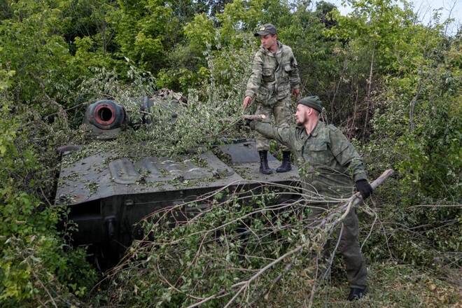 Service members of pro-Russian troops remove branches covering a self-propelled howitzer in the Luhansk region