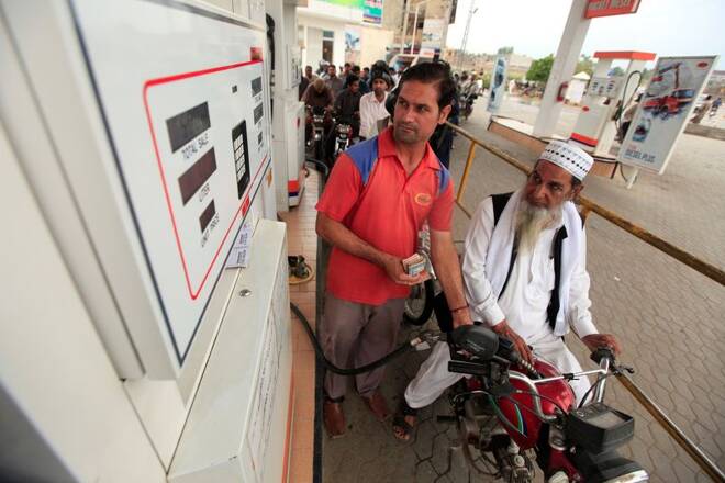 Motorcyclists wait in line as an attendant fiils the tank of a motorcycle at a petrol station in Rawalpindi