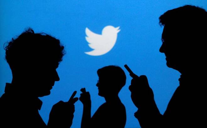 Smartphone users are silhouetted against a backdrop projected with the Twitter logo
