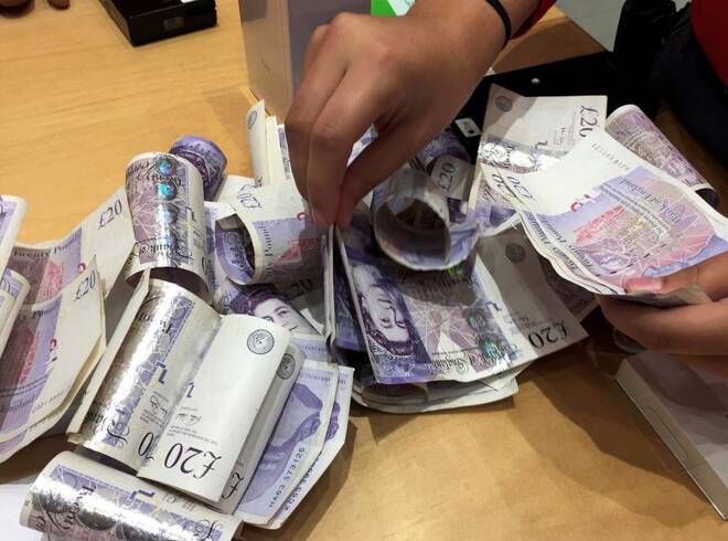 A shop assistant counts piles of British Pound Sterling banknotes at an Apple store in London