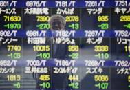 A man wearing a protective mask, amid the COVID-19 outbreak, is reflected on an electronic board displaying stock prices outside a brokerage in Tokyo