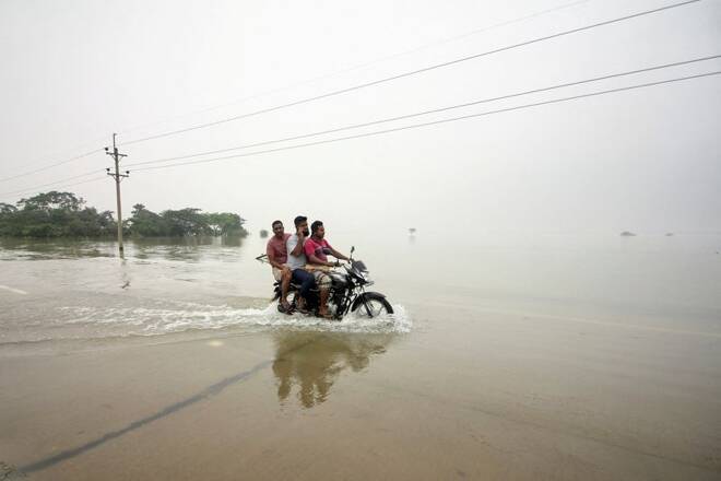 People ride on a bike on a submerged road during a widespread flood in Sylhet