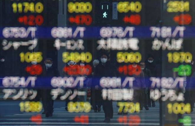 Pedestrians wearing protective masks are reflected on an electronic board outside a brokerage in Tokyo