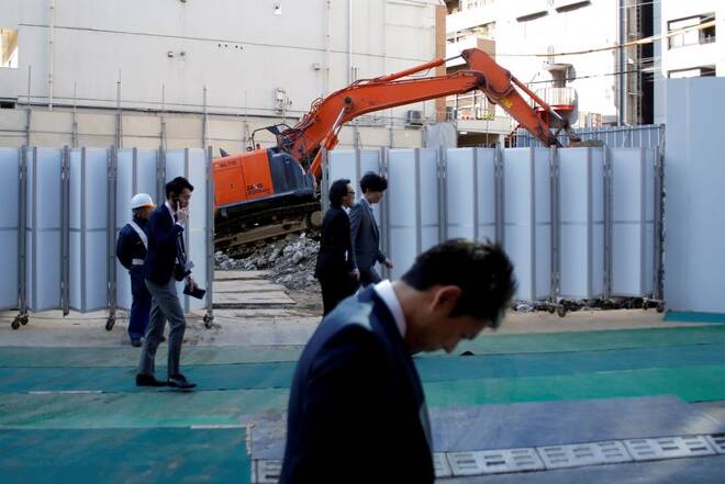 Businessmen walk past heavy machinery at a construction site in Tokyo's business district