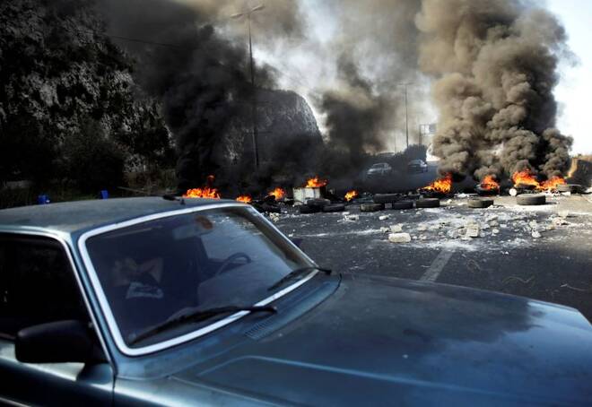 A man sleeps in a car next to burning tires barricading the highway during ongoing anti-government protests at Nahr El Kalb