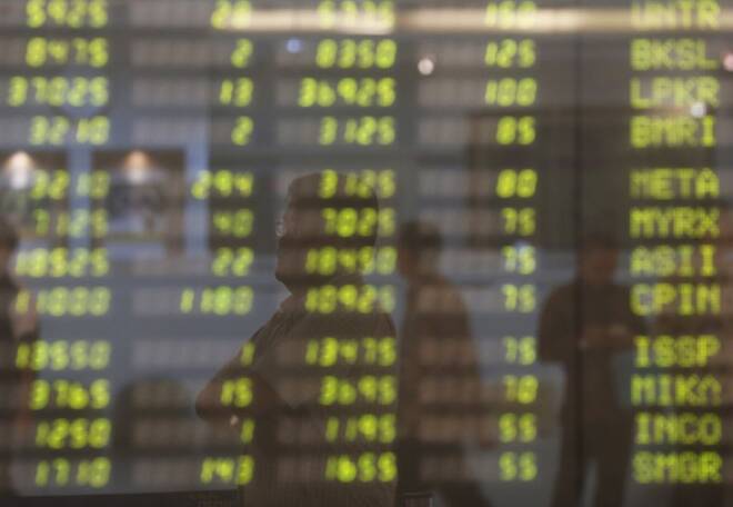 A man stands near electronic board showing stock market index at Bank Mandiri Sekuritas trading floor in Jakarta