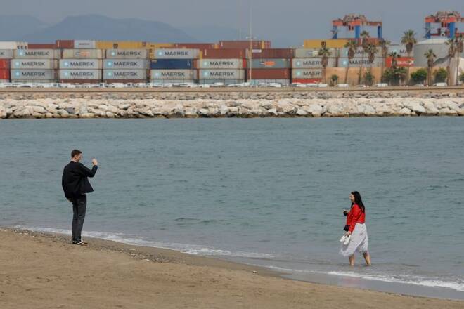 Tourists takes pictures on a beach in front of containers in a port in Malaga