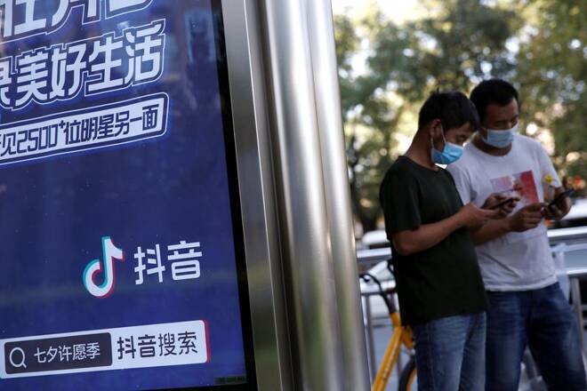People wearing face masks use smartphones next to an advertisement of TikTok (Douyin) at a bus stop in Beijing