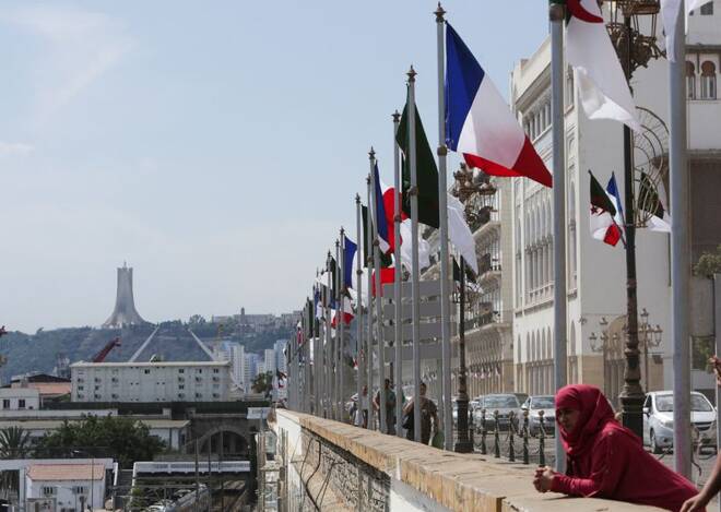 A woman stands near Algerian and French flags ahead of the arrival of French President Emmanuel Macron, in Algiers