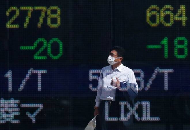 A man wearing a protective mask is reflected on an electronic board displaying stock prices outside a brokerage in Tokyo