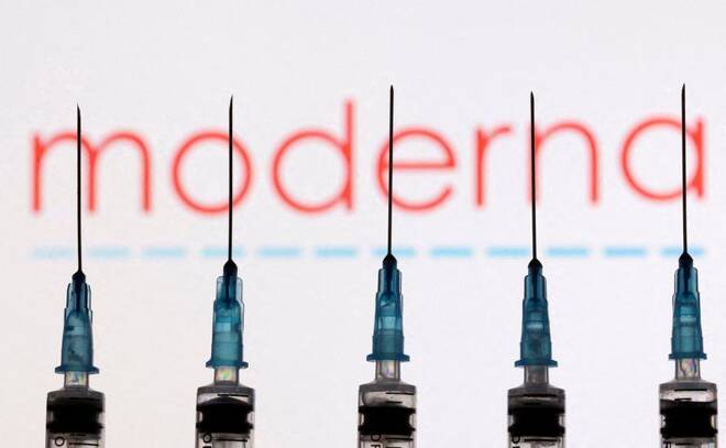 Syringes with needles are seen in front of a displayed Moderna logo in this illustration