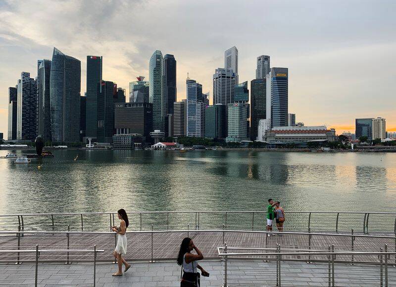 Passersby hold their mobile phones to take selfies with Singapore's central business district skyline in the background