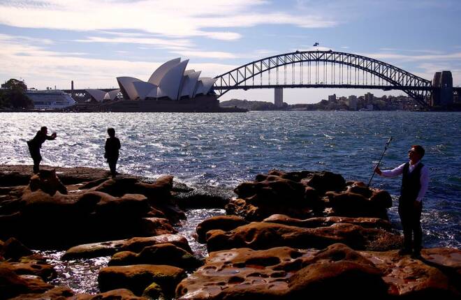 Tourists take photographs as they stand on rocks in front of the Sydney Harbour Bridge and Sydney Opera House