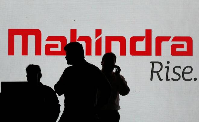 People walk past a screen displaying Mahindra and Mahindra logo before the start of a news conference in Mumbai