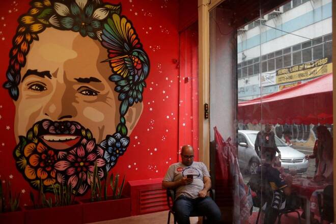 A man sits next to a graffiti of former Brazil's President and candidate for presidential election Luiz Inacio Lula da Silva at his campaign headquarters in Rio de Janeiro
