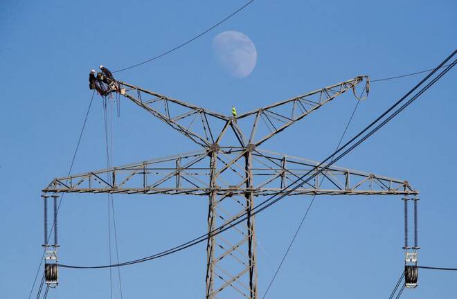The moon rises as electricians work atop a power pole near the lignite power plant of Neurath of German energy supplier and utility RWE, near Rommerskirchen