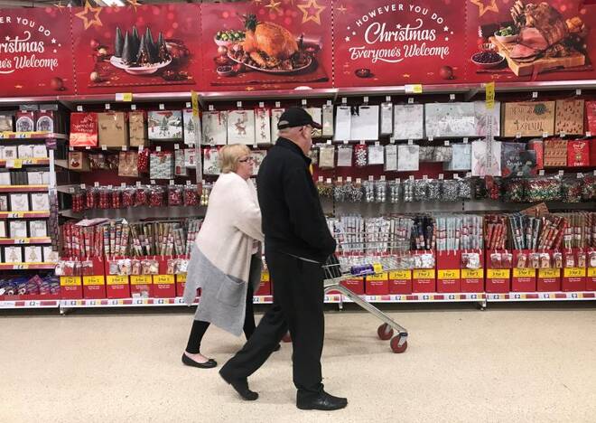 A woman pushes a shopping trolley past Christmas decorations for sale in a Tesco store in Manchester