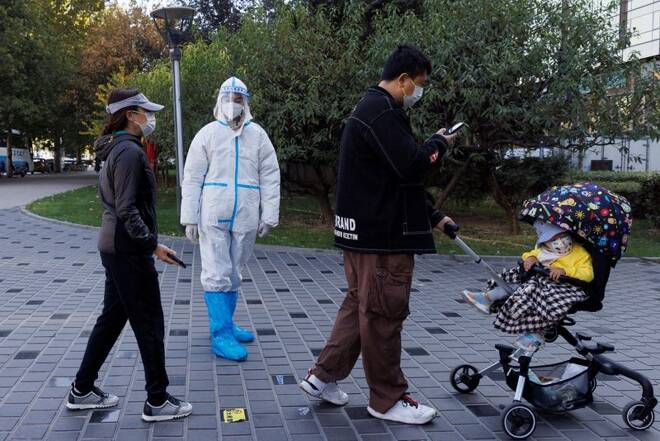 A pandemic prevention worker wears a protective suit as people line up to get swab tests at a testing booth as outbreaks of coronavirus disease (COVID-19) continue in Beijing