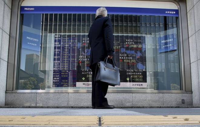 A pedestrian stands to look at an electronic board showing the stock market indices of various countries outside a brokerage in Tokyo