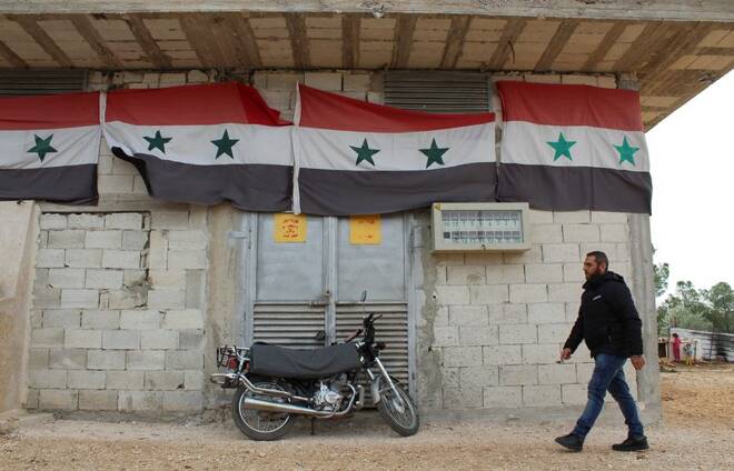 A worker walks past Syrian national flags at a solar farm in Hama