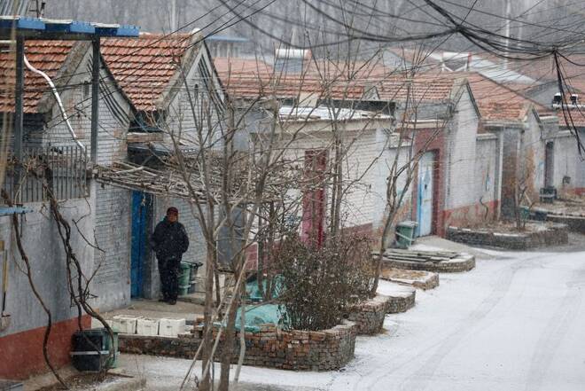 An elderly person stands outside a house amid snowfall in Beijing