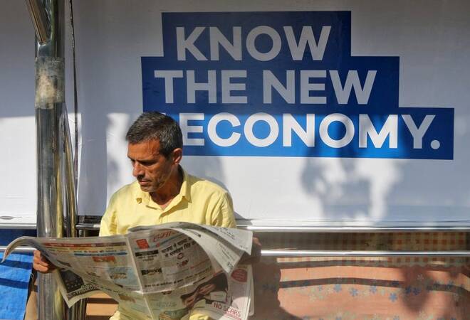 A man reads a newspaper as he waits for public transport at a bus stop in Mumbai