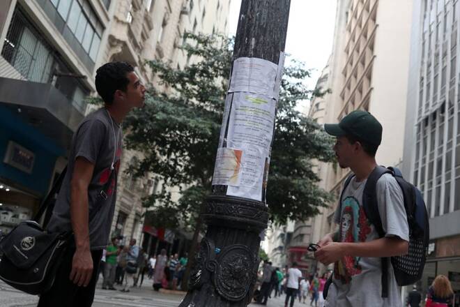Young men look at job listings posted on a street in Sao Paulo