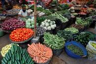 A vendor waits for customers to sell vegetables at a makeshift stall in a market, in Karachi