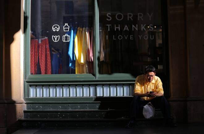 A shopper uses his phone as he sits outside a small retail clothing shop in Sydney, Australia