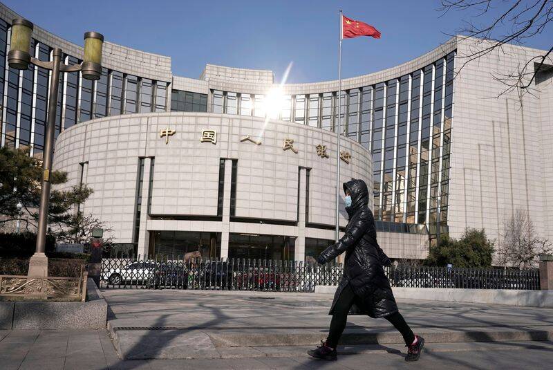 Man wearing a mask walks past the headquarters of the People's Bank of China, the central bank, in Beijing