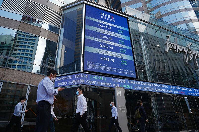 People walk past a screen displaying the Hang Seng stock index at Central district, in Hong Kong
